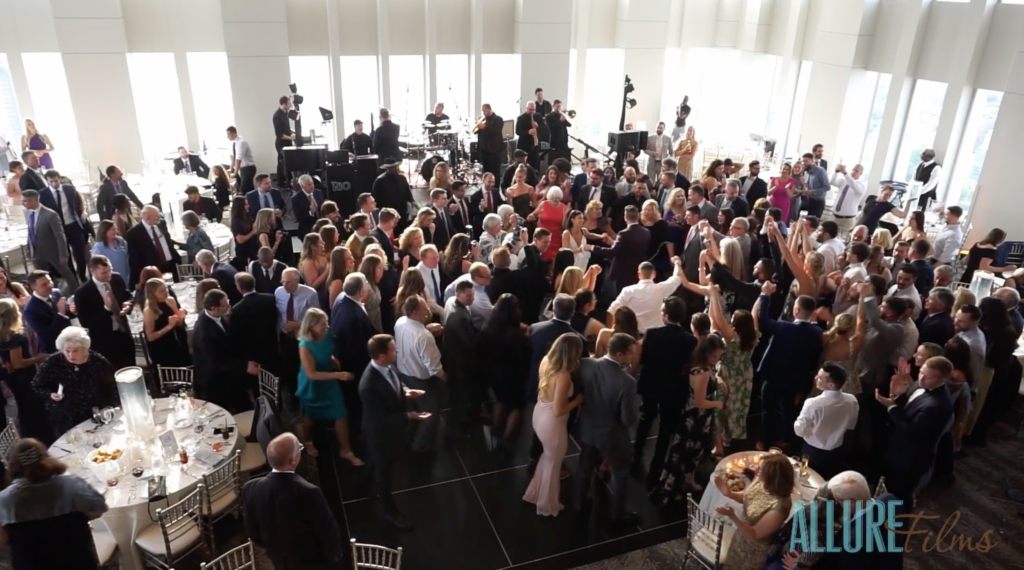 Vibrant wedding celebration at Vue on 50. Crowded reception room with dancing guests celebrating to a live wedding band.